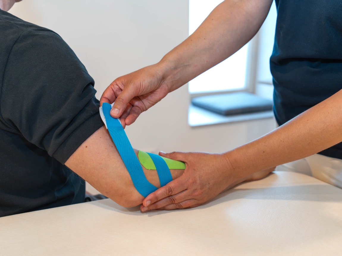 Anlegen eines Kinesio-Tapes am Ellenbogen einer Patientin